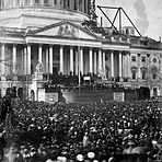 A large crowd in front of a large building with many pillars.