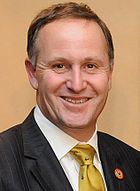 A smiling man wearing a white shirt with a green tie and black jacket