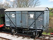 A short goods van built from planks of wood. The sides are mid-grey with a large white G to the left of the doors and a large white W to the right.