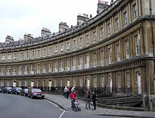 Semicircular terrace of 3 story buildings with matching windows and roofs, stone bands run the length of the terrace.