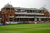 A brown colored pavilion in front of a green field, surrounded by a number of banners