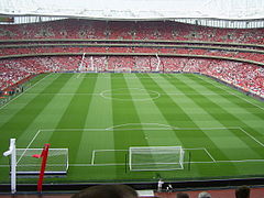 An interior view of a football stadium.  There are no players on the pitch but there are spectators in the stands.