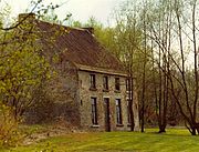 photo of a two-story brick house on the left partially obscured by trees with a front lawn and with a row of trees on the right