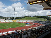 Interior de un estadio deportivo. There is a running track surrounding a central grassed area. In the distance there are the outer stands. In the foreground is the main stand, with plenty of people seated