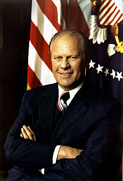 El presidente Gerald Ford, los brazos cruzados, frente a una bandera de Estados Unidos y el sello presidencial.