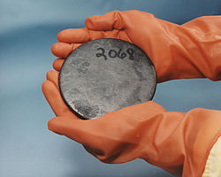 Dos manos en guantes marrones sosteniendo un disco gris manchada con un número 2068 escrito a mano en él