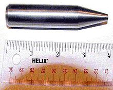 Cilindro metálico brillante con una punta afilada. La longitud total es de 9 cm y diámetro de unos 2 cm.
