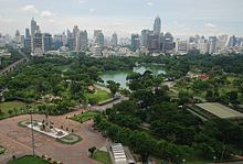 Un parque con muchos árboles y un lago; un bronce de pie delante de la estatua del parque; muchos edificios en el fondo