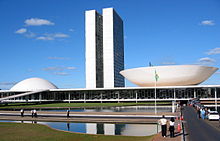 La vista muestra un edificio del siglo 20 con dos torres idénticas muy cerca de dos entre sí pasando de un edificio bajo que tiene una cúpula en un extremo, y una cúpula invertida, como un platillo, en el otro.