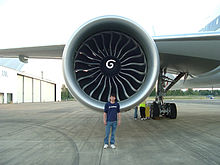 Motor de aviones, vista mirando hacia el frente con un ingeniero de Boeing delante para demostrar el tamaño del motor. Gran entrada circular del motor contiene un cubo central con una marca de remolino, rodeado de múltiples aspas del ventilador curvas.