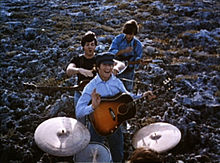 Los Beatles interpretando música en un campo. En primer plano, los tambores son interpretados por Starr (sólo la parte superior de la cabeza es visible). Detrás de él, los otros tres se destacan en una columna con sus guitarras. En la parte trasera, Harrison, la cabeza hacia abajo, toca la fibra sensible. En la parte delantera, Lennon le sonríe y le da un poco de onda hacia la cámara, la celebración de su selección. Entre ellos, McCartney es jocosamente a punto de ahogarse Lennon.