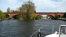 un ladrillo rojo puente construido con arcos de poca profundidad que atraviesa un río, visto desde la parte frontal de un pequeño barco