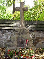 A stone cross atop a large rock. A plaque mounted on the rock reads: