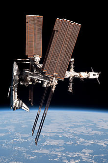 A side-on view of the ISS showing a Space Shuttle docked to the forward end, an ATV to the aft end and Soyuz & Progress spacecraft projecting from the Russian segment.