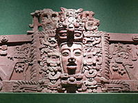 Sección de friso de estuco con rostro humano prominente en el centro, rodeado de elaborada decoración.