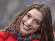 Un tiro en la cabeza de una mujer joven mirando hacia la cámara y sonriendo. Ella lleva una chaqueta roja y una bufanda y la nieve está cayendo en el fondo y el aterrizaje en el pelo.