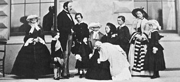 Photo d'une Victoria assis, v??tu de noir, tenant un nourrisson avec ses enfants et Prince Albert debout autour d'elle.