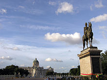 Une grande place avec une statue en bronze d'un homme sur un cheval dans le centre; au-del?? de la place est un grand b??timent de deux ??tages avec un toit en forme de d??me, fen??tres cintr??es et des colonnes