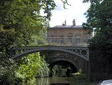 Un pont de fer enjambant l'eau. Dans l'arri??re-plan est un b??timent en pierre jaune. Sur la m??che gauche atteindre sur l'eau.