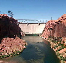 Un barrage presque blanc se ??tend ?? la roche de couleur rouge de chaque c??t??. An arching steel bridge crosses in front of the dam.