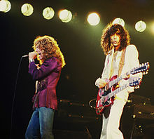 Une photographie en couleur de Robert Plant avec microphone et Jimmy Page avec une guitare ?? double col sur sc??ne.