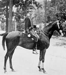 Photo en noir et blanc d'un cavalier en uniforme sur son cheval monté en bride présentant son profil droit.