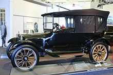 Voiture du début du XXe siècle avec un toit décapotable et un pare-brise vertical.