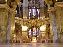 Photographie de l'intérieur d'une chapelle de style roman avec un large lustre doré suspendu au-dessus d'un autel.