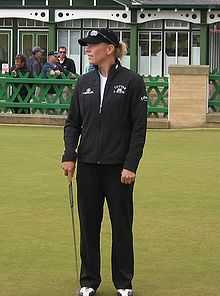 Golfeuse, debout, avec une casquette, et tenant un club dans la main droite.