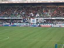 vue d'une tribune derrière un but, les supporters brandissant des drapeaux.