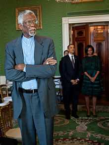 Bill Russell dans un salon de la Maison Blanche. Le président Barrack Obama et sa femme sont présent derrière lui.