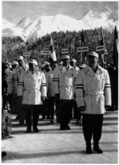 Un groupe d'hommes, devant des drapeaux et, en arrière-plan, des montagnes