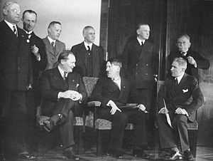 Photograhie en noir et blanc des membres du cabinet d'Adolf Hitler, prise le 30 janvier 1933. Au premier plan, de gauche à droite, Hermann Göring, Adolf Hitler et Franz von Papen sont assis sur des fauteuils. Les jambes croisées, les mains sur le genou, Göring, d'assez forte corpulence, a le visage souriant, tourné ver Adolf Hitler. À sa droite, au centre de l'image, Hitler est immédiatement reconnaissable, avec la mèche de cheveux qui lui barre le front et sa petite moustache en brosse ; il a la main droite posée sur son genou et tient des documents de la main gauche. À droite de l'image, Franz von Papen, dressé sur son siège, regarde vers les deux hommes. Tous les membres du cabinet sont en civil et vêtus d'un costume sombre, à l'exception de von Krosig (debout, troisième en partant de la gauche de l'image) qui porte un costume plus clair. Sur le revers gauche du veston de Göring et Hitler, on distingue l'insigne du parti nazi