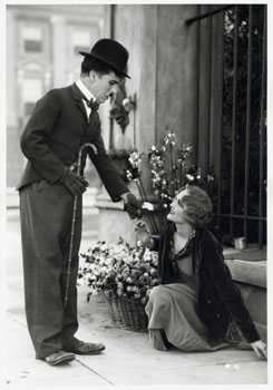 Capture d'écran montrant Charlot tendant la main à une jeune femme assise dans la rue à côté de bouquets de fleurs.