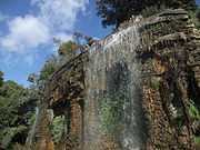 Vue de trois-quarts d'une cascade de quelques mètres de hauteur et de largeur dans un parc sous un ciel bleu.