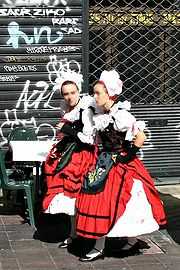 Vue de 2 jeunes filles en habitant traditionnel tranchant avec la grille de magasin verte fermée et taguée en fond.