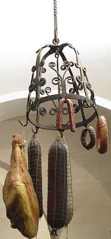 Une couronne d’office en fer forgé formant un dôme ajouré, décoré de volutes, est suspendue par une barre de fer torsadé au plafond en voute blanche du Musée de la Gourmandise ; un gros jambon et des saucissons de tailles diverses sont attachés à ses crochets par des ficelles.