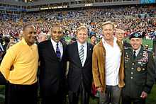 Photographie montrant, de gauche à droite, Lynn Swann, Roger Craig, Roger Goodell, John Elway et le général David Petraeus devant une foule de spectateurs