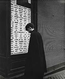 Photographié par Emil Mayer (de), homme observant des timbres-poste de collection proposés à la vente dans la vitrine d'un négociant spécialisé, à Vienne (Autriche), entre 1905 et 1914.