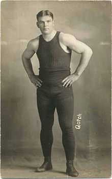 Photographie en noir et banc de Frank Gotch portant un pantalon noir et un marcel noir.