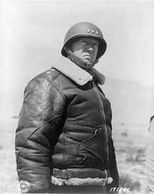 Portrait en contre-plongée de Patton portant un casque avec trois étoiles sur le devant et une veste de cuir rembourrée.