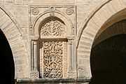 Photographie d’un panneau sculpté de la façade du portique occidental de la cour. Ce panneau en pierre est orné d’un décor symétrique de rinceaux et de fleurs, se terminant par un croissant.