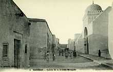 Photographie d’époque, vers 1900, montrant la façade occidentale de la Grande Mosquée de Kairouan. Les façades de l’édifice étaient entièrement badigeonnées à la chaux, avant les restaurations des années 1960.