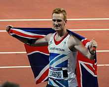 Photographie de Greg Rutherford portant le drapeau britannique