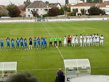 Présentation des équipes, alignées sur un seul rang. Les trois arbitres séparent les deux équipes.