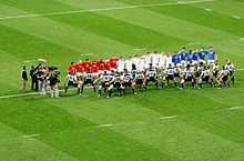 McCaw et les Néo-Zélandais en maillot gris interprètent le haka face aux joueurs français vêtus de bleu, blanc et rouge.