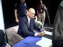 Homme assis à une table, signant des livres.