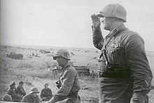 Photo en noir et blanc d'hommes en uniforme avec au second plan des chars de combat.