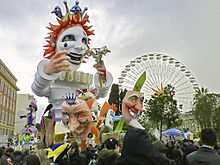 Vue d'un char de carnaval avec des masques au premier plan et une grande roue en fond.