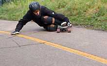 Longboarder descendant une route ici en virage. Il pose une main et un genou par terre.